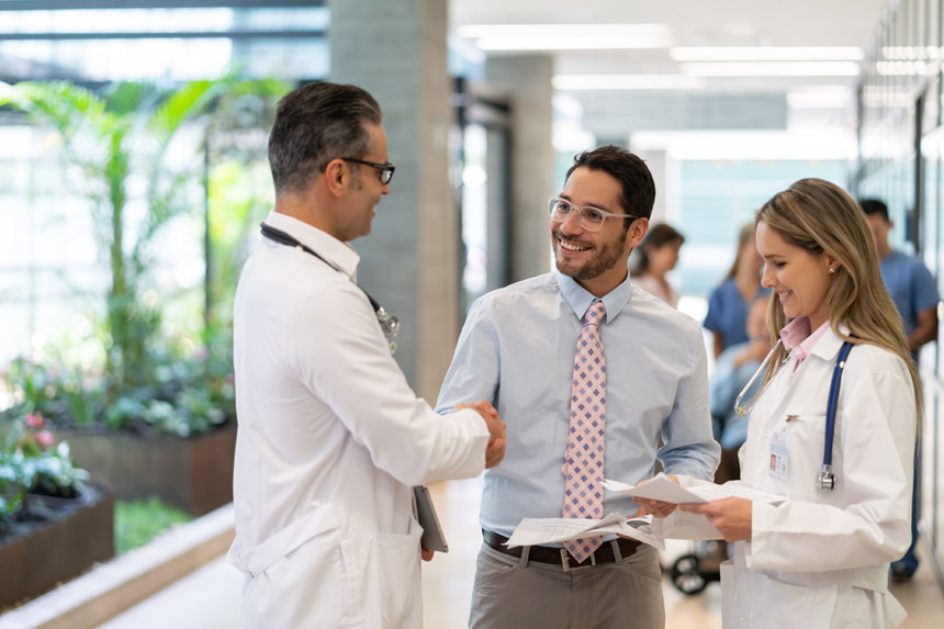 A medical science liaison smiles as he interacts with two healthcare professionals in a medical facility hallway.