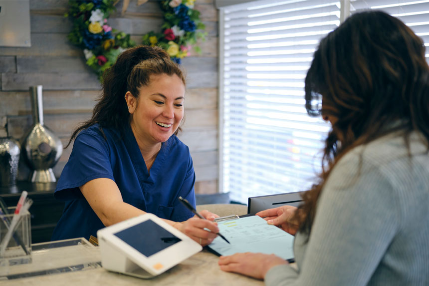 A medical receptionist smiles as she helps a patient review their invoice.