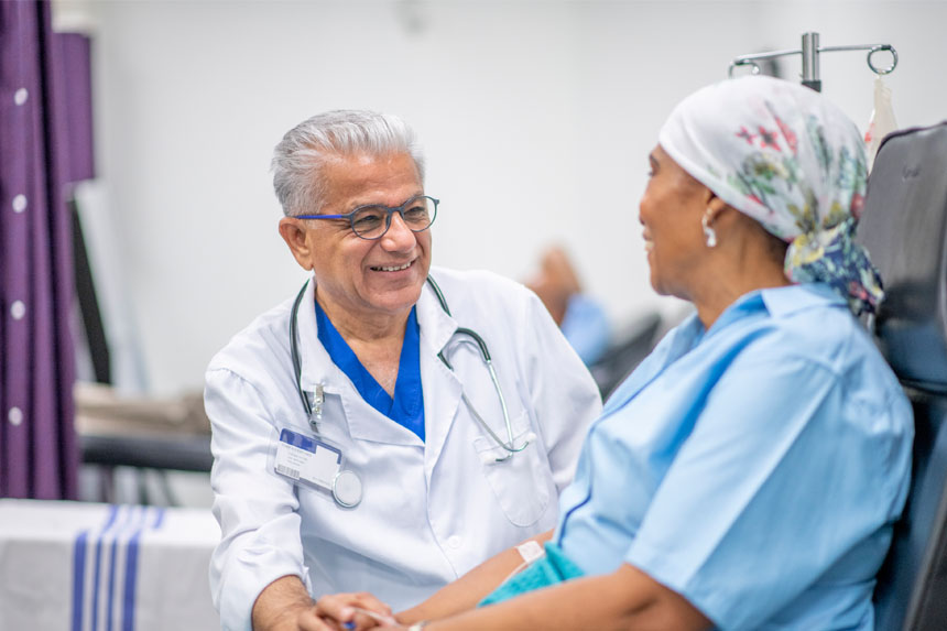 healthcare professional smiles while touching the hand of a patient who is sitting down